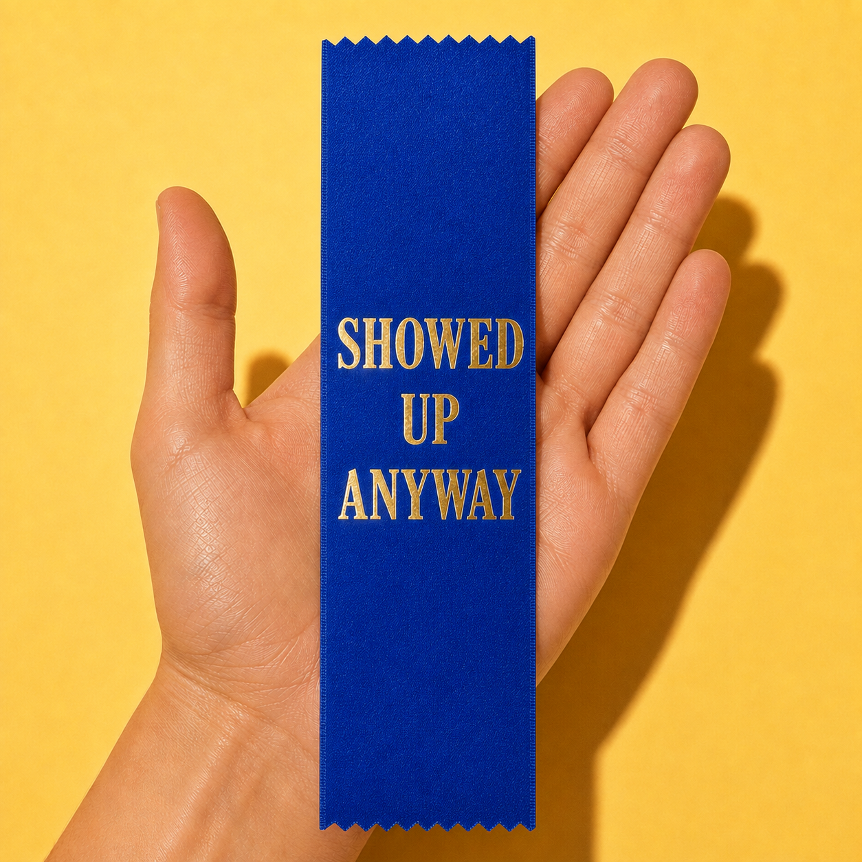 Blue gold-foil ribbon saying SHOWED UP ANYWAY, with pinked zigzag ends; illustrative mockup